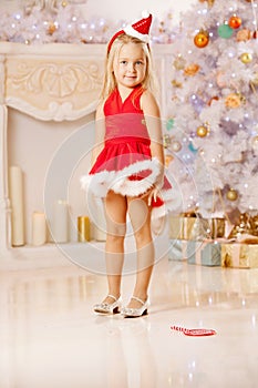 Beautiful little Santa girl near the Christmas tree. Happy gir