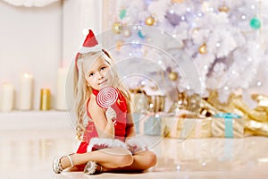 Beautiful little Santa girl near the Christmas tree. Happy girl