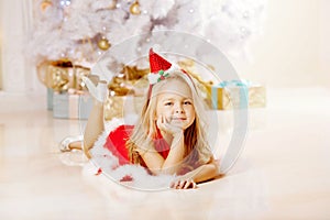 Beautiful little Santa girl near the Christmas tree. Happy girl
