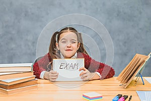 A beautiful little schoolgirl is sad and overwhelmed. Conducting paper with text exam. Written sitting at the school