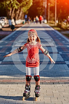 Beautiful little sportive girl skating in the rollers in the city park in summer season.