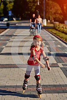 Beautiful little sportive girl skating in the rollers in the city park in summer season.