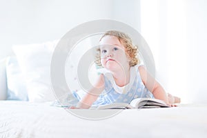 Beautiful little toddler girl with curly hair reading book