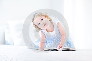 Beautiful little toddler girl with curly hair reading book