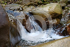 Beautiful little waterfall in mountains. Water flows between stones