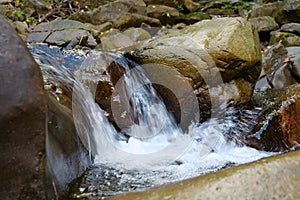 Beautiful little waterfall in mountains. Water flows between stones