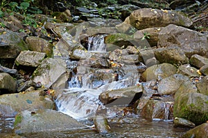 Beautiful little waterfall in mountains. Water flows between stones