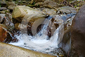 Beautiful little waterfall in mountains. Water flows between stones