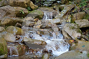 Beautiful little waterfall in mountains. Water flows between stones