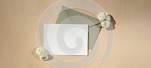 Beautiful little white flowers on postal green envelope on beige background, empty paper note copy space for text