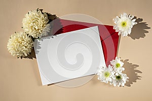 Beautiful little white flowers on postal red envelope on beige background, empty paper note copy space for text, spring