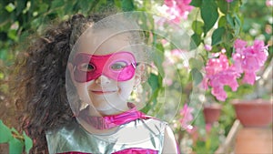 Beautiful llittle girl in the superhero costume, dressed in a pink cloak and the mask of the hero. Plays on the