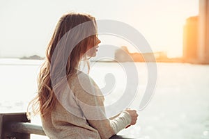 Beautiful lonely girl dreaming and thinking while waiting for date in the city ocean pier at sunset time.