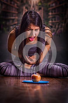 Beautiful and lonely girl suffering from anorexy, suffering pain in his stomach when she looks an apple over a blue