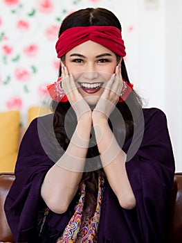 A beautiful long black hair lady with a red turban and purple blanket is sitting and smile with elegant gesture on a big dark