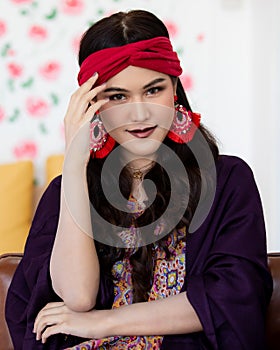 A beautiful long black hair lady with a red turban and purple blanket is sitting and smile with elegant gesture on a big dark