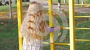 Beautiful long blonde hair girl holds yellow leaves on nature background. Smiling child plays in autumn park sunny day