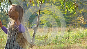 Beautiful long blonde hair girl holds yellow leaves on nature background. Smiling child plays in autumn park sunny day