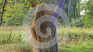 Beautiful long blonde hair girl holds yellow leaves on nature background. Smiling child plays in autumn park sunny day