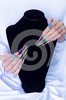 Beautiful long colorful false nails on a white background and black base , the nails for the exhibition