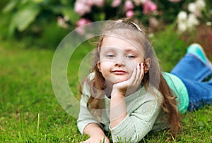 Beautiful long curly hair kid girl lying on green grass in fashi