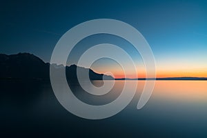 Beautiful long exposure sunset over a calm lake with mountain silhouette and fading light