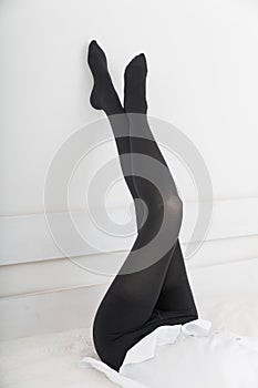 Beautiful long female legs in stockings. Girl putting on stockings at home in a white room. Black tights. Varicose veins