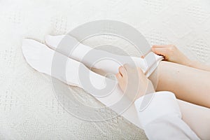 Beautiful long female legs in stockings. Girl putting on stockings at home in a white room. White hosiery. Varicose