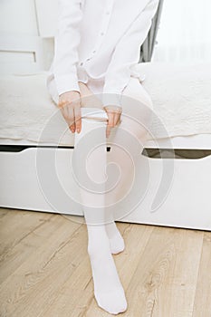 Beautiful long female legs in stockings. Girl putting on stockings at home in a white room. White hosiery. Varicose