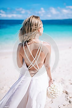 Beautiful long hair bride in long white dress standing on the beach with white bouquet loking to the sea
