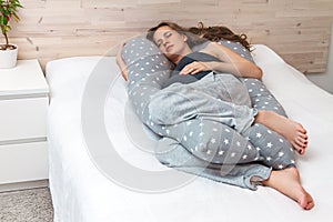 Beautiful long hair pregnant  woman with big abdomen,  sleeping on body& x27;s pillow  on the sofa indoors .