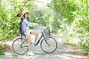 Beautiful long-haired Asian woman riding a bike in a community forest park along a nature trail to breathe fresh air Smiling