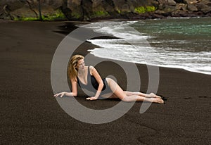 Beautiful and long haired blonde woman lays on black sand beach in black swimsuit in Azores, Portugal