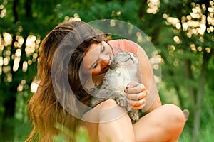 Beautiful long-haired brunette girl in a park sitting with a cat. The girl growls at the cat and bites. Photoshoot with a pet cat