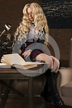 Beautiful long haired curly blonde schoolgirl tiredly learns homework in a classic vintage interior room, sitting at a table