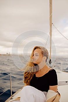 A beautiful long-haired girl sits on the bow of a barred yacht and enjoys life. The blonde is resting in the open sea or ocean.