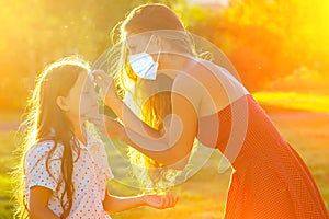 Beautiful long-haired mother in cocktail red dress wipes her daughter`s hands with wet hygienic napkins in the park in