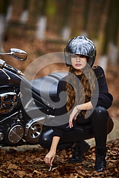 A beautiful long-haired woman smoking on a chopper motorcycle in autumn landscape.
