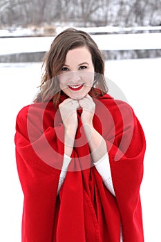 Beautiful long haired woman in vintage red cape riverside in winter