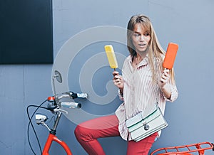 Beautiful long-haired young blonde woman makes a choice of ice cream sitting on a red vintage bike