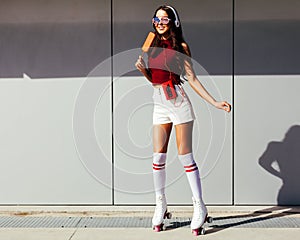 Beautiful long-legged asian girl skating in roller skates and enjoying an ice cream on a summer day