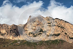 Beautiful long pointed rock is illuminated by the sun. Sunny mountain landscape with high sharp rockies under white clouds.