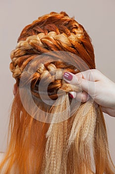 Beautiful, with long, red-haired hairy girl, hairdresser weaves a braid, close-up in a beauty salon.