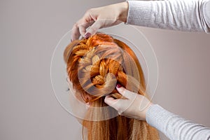 Beautiful, with long, red-haired hairy girl, hairdresser weaves a braid, close-up in a beauty salon.