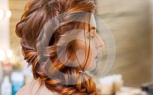 Beautiful, with long, red-haired hairy girl, hairdresser weaves a French braid, in a beauty salon.