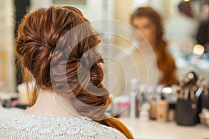 Beautiful, with long, red-haired hairy girl, hairdresser weaves a French braid, in a beauty salon.