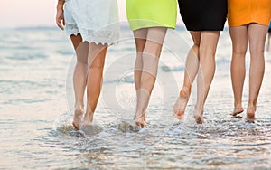 Beautiful, long and smooth women`s legs walk on the sand near the sea. Girls on the summer beach. Beautiful legs of girls.