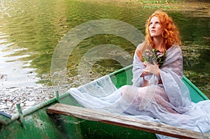 Beautiful longing young sexy woman, redhead with red hair, bride, with a bouquet of flowers in a boat