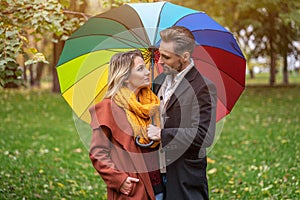 Beautiful in love couple standing in the park under a rainbow colored umbrella looking at each others eyes. A beautiful