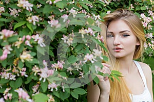 Beautiful lovely girl with long blonde hair enjoying nature near blooming rosebush in a white t-shirt with full lips bright summer